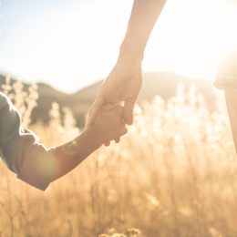 Mother little child holding hands walking in a grass field at su